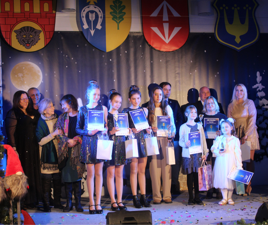 Grupa laureatów na scenie z dyplomami i nagrodami rzeczowymi na scenie w otoczeniu organizatorów