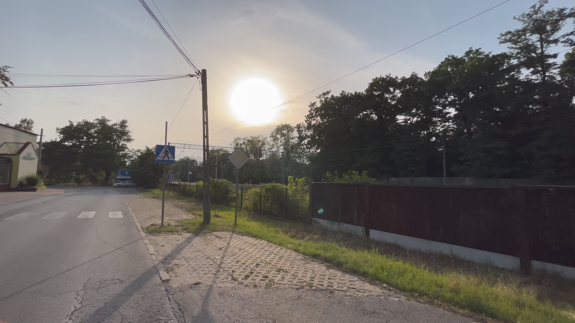 ul. Warszawska i pas zieleni, widoczne ogrodzenie torów kolejowych, na drugim planie zachodzące słońce